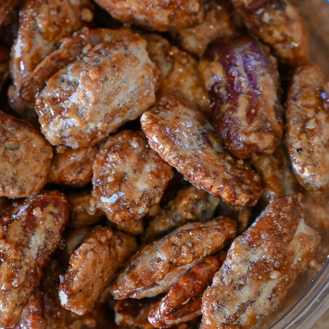 Close-up of glazed almonds coated in a glossy brown sugar and spice glaze, piled together in a clear container.