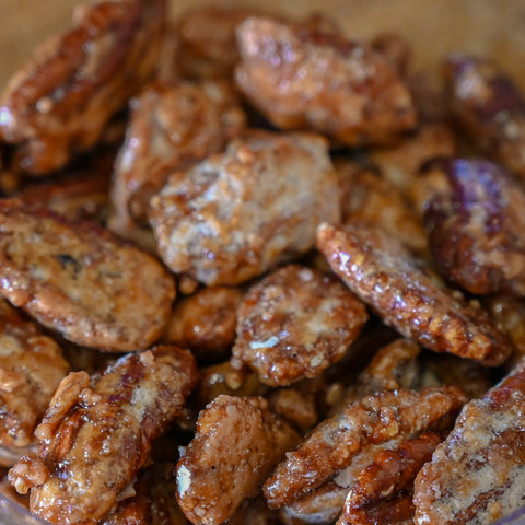 A close-up shot of glazed pecan halves piled together, showing a glossy, caramelized brown finish.