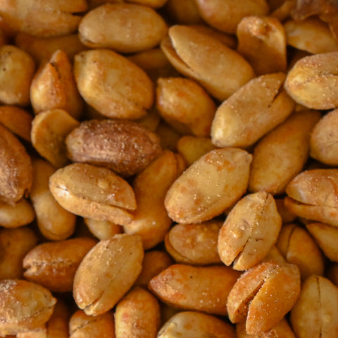 A close-up pile of roasted peanuts with a light dusting of seasoning, filling the entire frame.