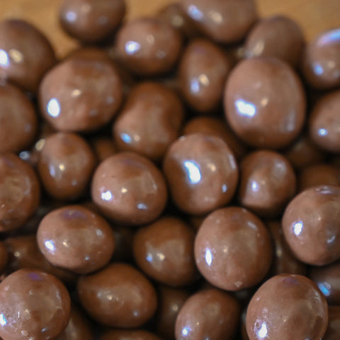 A close-up pile of glossy brown chocolate-covered raisins with a clear background.