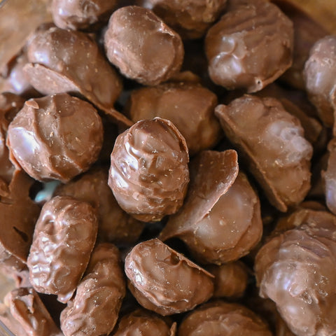 A close-up pile of chocolate-covered peanut nut clusters, showing the glossy brown coating and textured nut surfaces.