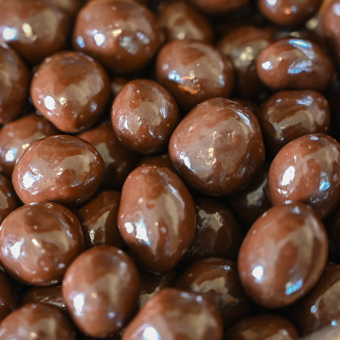 A close up photo of glassy, chocolate covered chocolate peanuts entirely filling the frame.