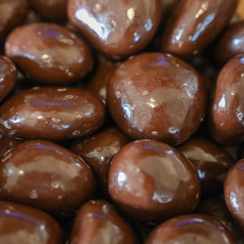 A close-up pile of glossy brown chocolate-coated cherries filling the frame.