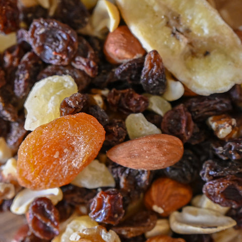 Close-up of a mixed snack blend containing dried banana slices, raisins, almonds, and apricots.