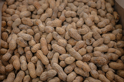 A close-up view of many whole peanuts in their natural tan-brown shells, filling the frame.