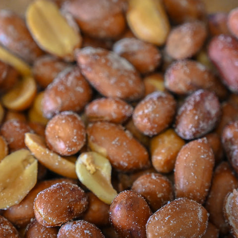Close-up of roasted peanuts with some split shells showing pale tan interiors, lightly dusted with salt crystals.