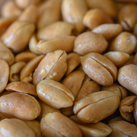 A close-up shot of roasted peanuts filling the frame, showing their golden-brown, glossy peels.