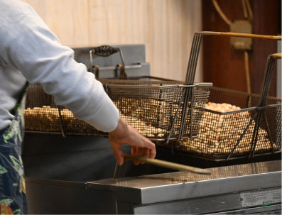 Person operating a deep fryer with multiple baskets of peanuts
