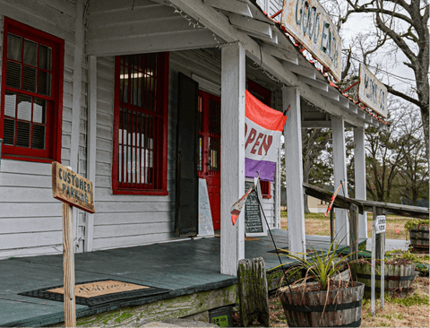 Front porch of a small building with a 'Open' sign and various signs on a wooden post.