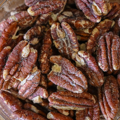 Close-up of salt-coated pecans piled together in a clear container.