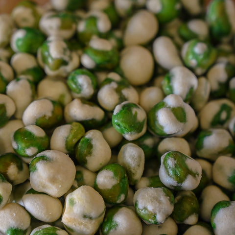 A close-up shot of green and white wasabi covered peas piled together.