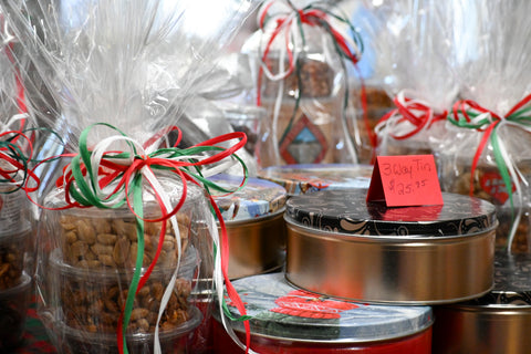 A close-up of assorted gift baskets and tins wrapped in clear cellophane and tied with red, white, and green ribbons, with a small red price tag reading $20.00 on one tin.