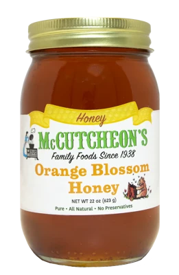 A glass jar of McCutcheon's Orange Blossom Honey with a gold metal lid and a white label, shown against a plain white background.